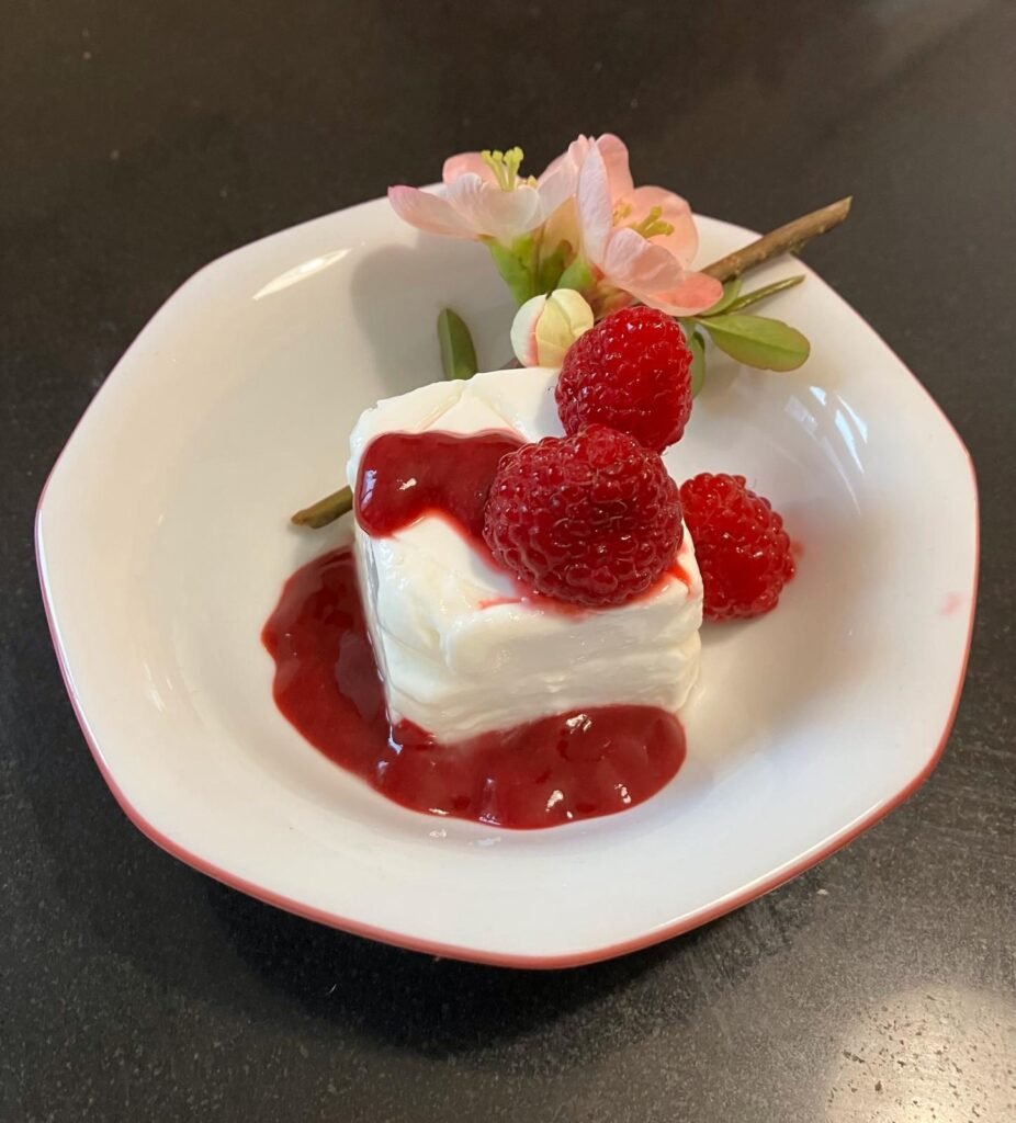 Goat’s milk dessert topped with raspberry coulis, with fresh raspberries and quince blossom